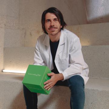 Estudante de mestrado da Universidade de Vigo cunha bata branca e unha caixa verde nas mans